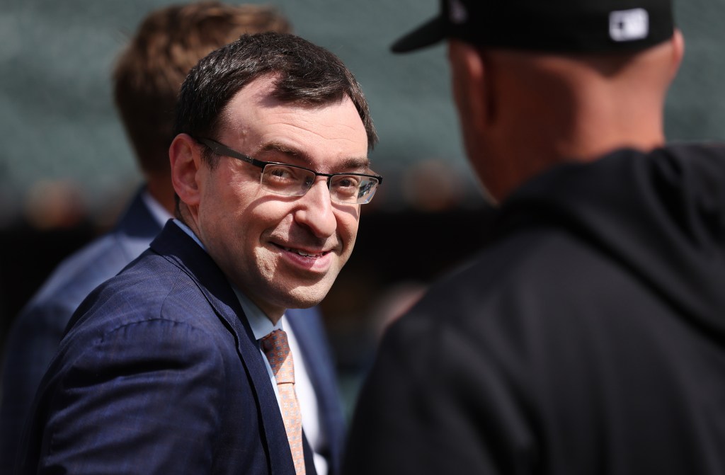 Man wearing glasses and a blue suit smiling at someone whose back is to the camera.