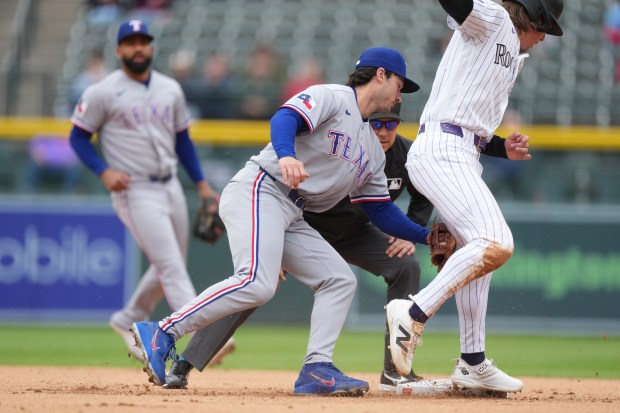 Texas Rangers second baseman Justin Foscue, center, applies a late tag as Colorado Rockies' Jake McCarthy steals second base in the first inning of a baseball game Wednesday, May 20, 2026, in Denver. (AP Photo/David Zalubowski)