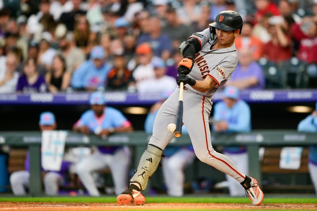 A San Francisco Giants player in grey and orange uniform hits a baseball.