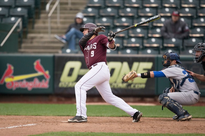 A baseball player in a maroon jersey swings his bat during a game