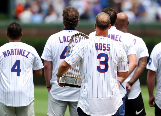 Former Cubs catcher and manager David Ross holds the 2016 World Series trophy while standing beside his former teammates during the national anthem before a game against the Twins on July 18, 2026, at Wrigley Field. (Chris Sweda/Chicago Tribune)