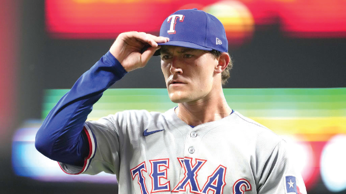 Texas Rangers player in gray uniform tipping his blue cap with a white 'T' while on the field