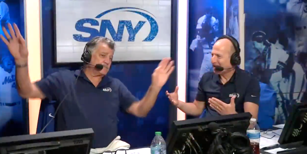 Two men in headphones and microphones, wearing blue SNY shirts, gesturing while broadcasting.