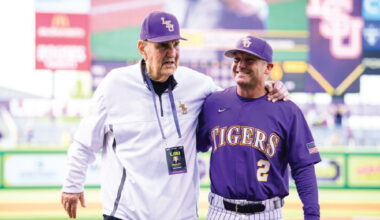 LSU Tigers baseball coach and player pose together on the field, with the player wearing a purple jersey that reads TIGERS and number 2