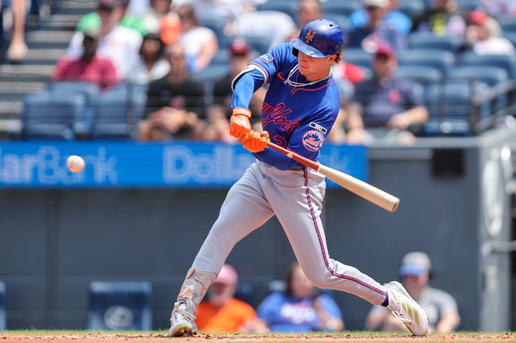 A baseball player in a blue Mets uniform swings a bat, hitting a baseball.