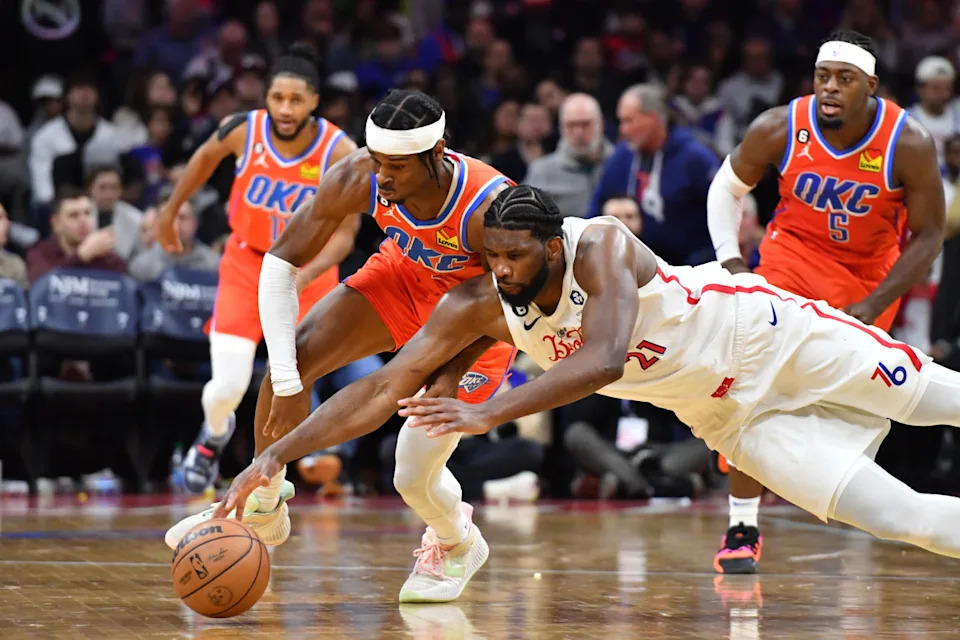Jan 12, 2023; Philadelphia, Pennsylvania, USA; Oklahoma City Thunder guard Shai Gilgeous-Alexander (2) dives for loose ball with Philadelphia 76ers center Joel Embiid (21) during the fourth quarter at Wells Fargo Center.© Eric Hartline-Imagn Images