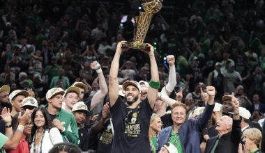 Jayson Tatum holding up a championship trophy while surrounded by other members of the Boston Celtics team.