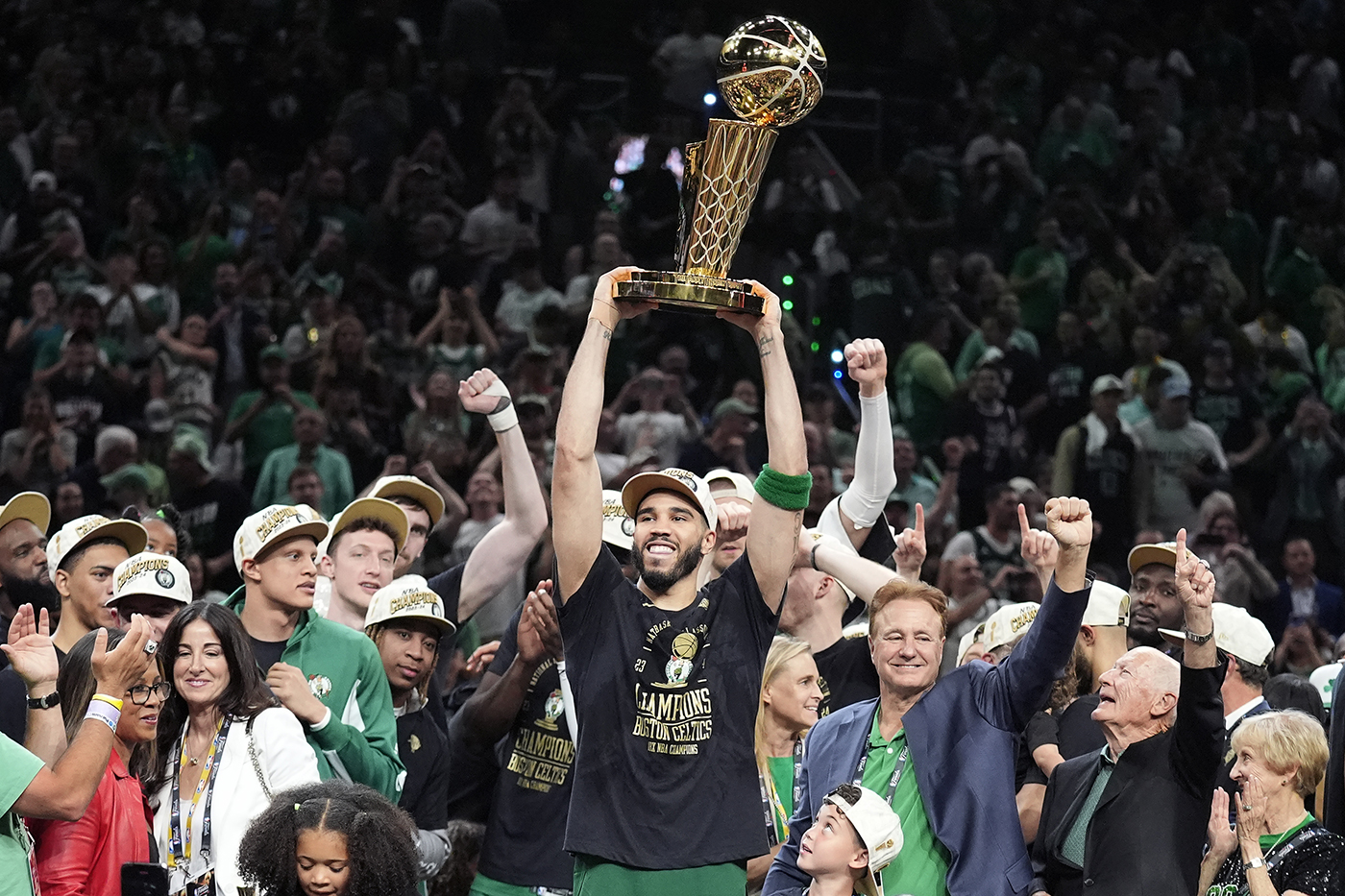 Jayson Tatum holding up a championship trophy while surrounded by other members of the Boston Celtics team.