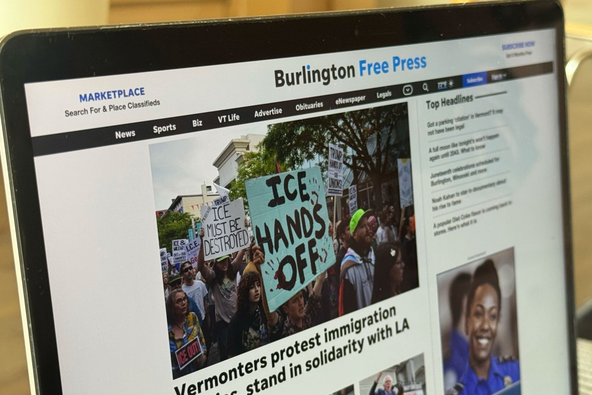 A laptop screen displays the Burlington Free Press website featuring a news article about a protest with people holding signs reading “ICE Hands Off” and “ICE Must Be Dismantled.”.