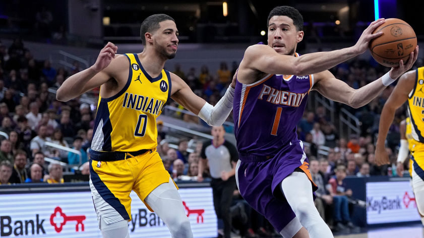Devin Booker #1 of the Phoenix Suns dribbles the ball while being guarded by Tyrese Haliburton #0 o...