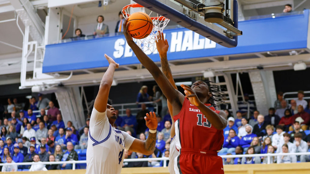 Rasheer Fleming #13 of the Saint Joseph's Hawks puts up a shot against Elijah Hutchins-Everett #4 a...