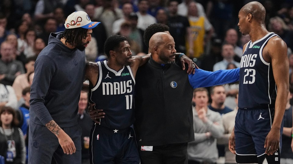 Kyrie Irving (11) being helped off the court after an injury, assisted by Anthony Davis and a staff member.