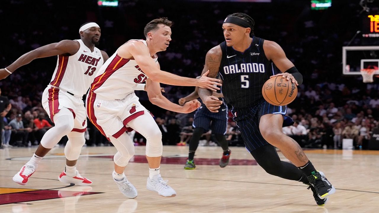 Magic forward Paolo Banchero (5) drives to the basket against Heat forward Duncan Robinson (55) and center Bam Adebayo (13) during the first half of Orlando's victory in their first game of the 2024-25 NBA season on Wednesday, Oct. 23, 2024, in Miami. (AP Photo/Wilfredo Lee)