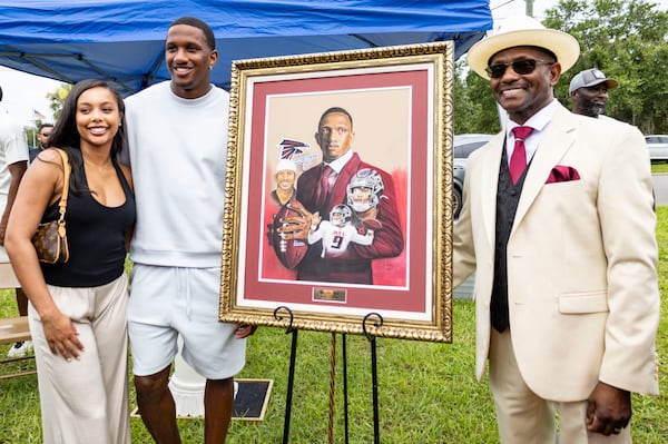 Artist Jerry Farmer (right) presents a painting to Falcons quarterback Michael Penix Jr. and his fiancee, Olivia Carter, during a recent street-naming ceremony in Penix's hometown of Dade City, Fla.