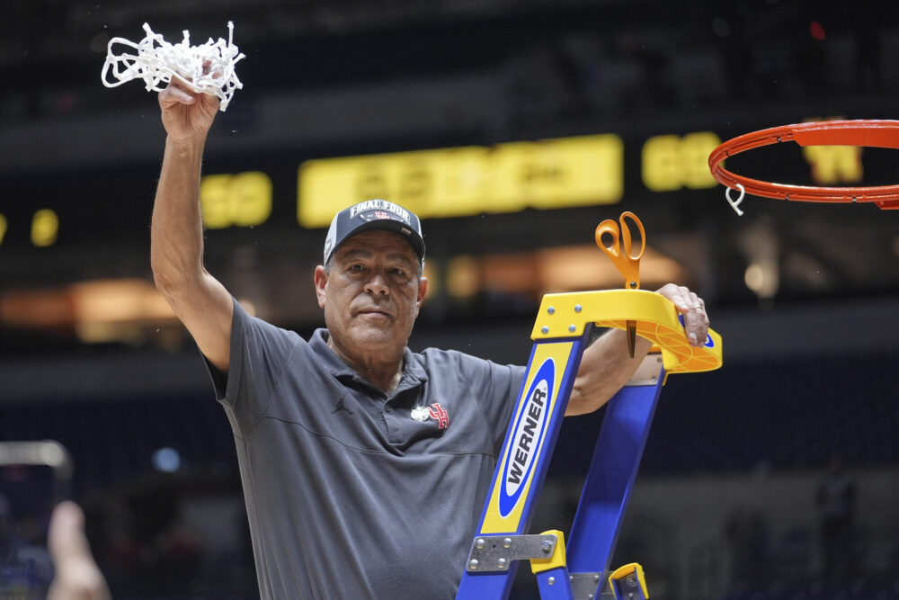  A man on a ladder hold up a net he cut off of a basket ball goal.
