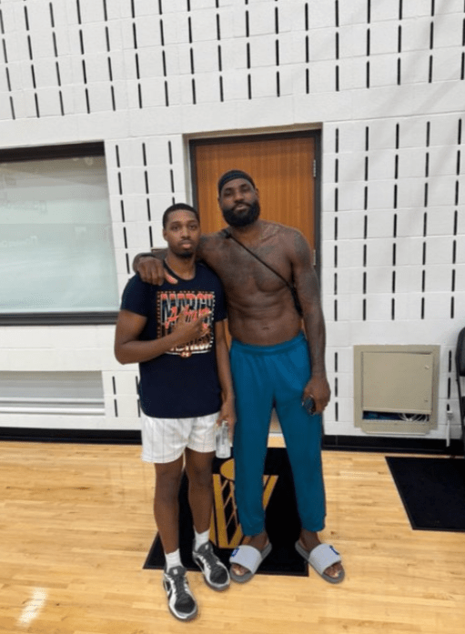 Two men posing for a photo; one shirtless, the other in a t-shirt and shorts.