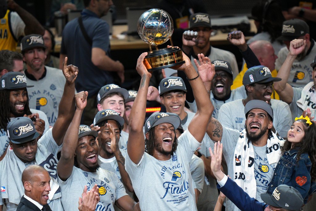 A crowd of Pacers basketball players cheer as the one in the center raises a trophy over his head.