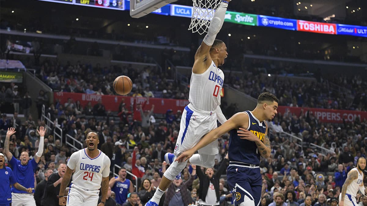 Los Angeles Clippers guard Russell Westbrook (0) hangs on the rim after a dunk over Denver Nuggets forward Michael Porter Jr. (1) in the first half at Crypto.com Arena.