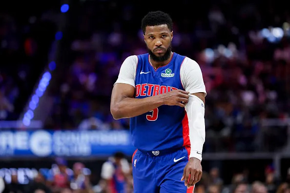 A basketball player in a Detroit Pistons jersey adjusts his arm sleeve on the court during a game.