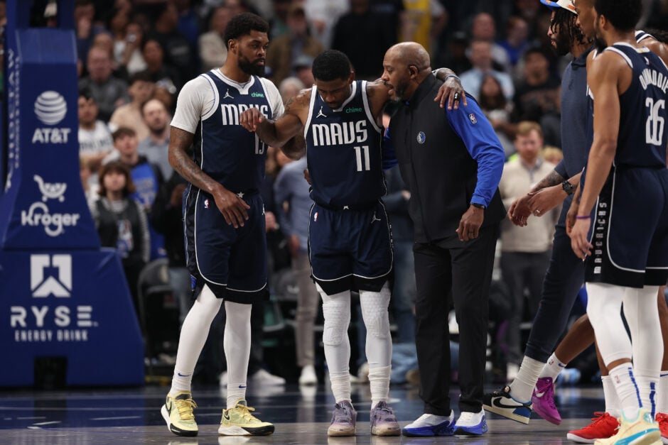 Kyrie Irving #11 of the Dallas Mavericks is helped off the court by Naji Marshall #13 and a team staff member after suffering an injury during the first half to Kings at American Airlines Center.