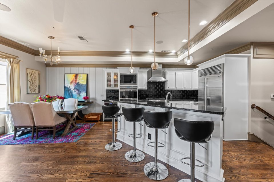 Interior view of a kitchen and dining area with hardwood floors, white cabinets, and a granite countertop.
