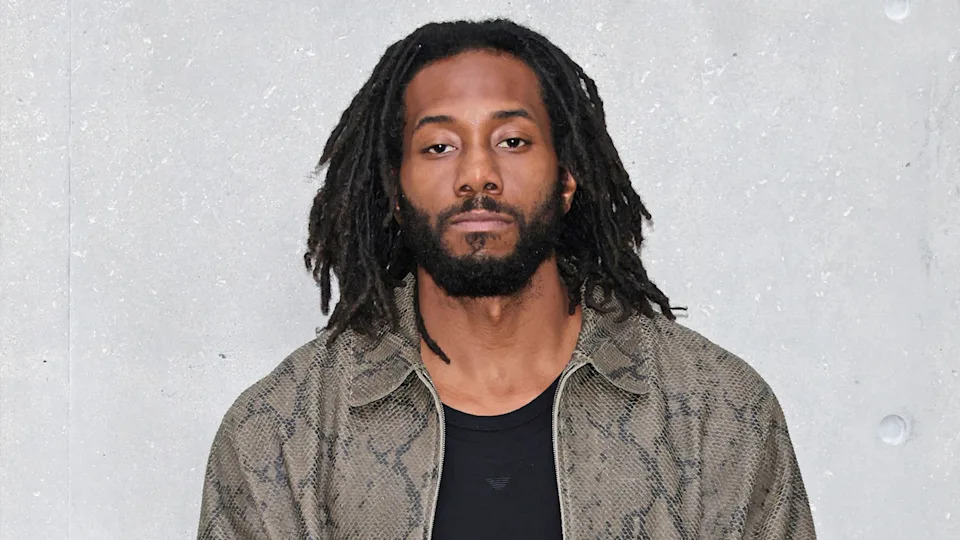 Kawhi Leonard wearing a snakeskin-patterned jacket, standing against a gray concrete wall.
