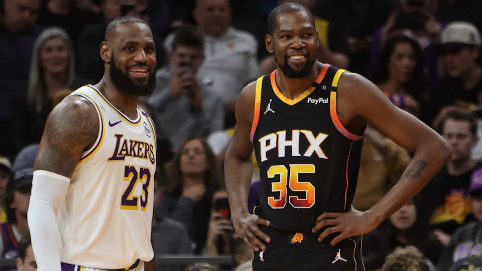 LeBron James in a Lakers jersey and Kevin Durant in a Suns jersey smiling on a basketball court.