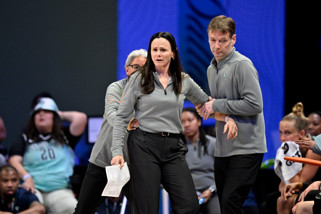 Two New York Liberty staff members pull New York Liberty head coach Sandy Brondello backward after Brondello received a technical foul. One staff member holds Brondello's hips, and the other grabs her elbow.