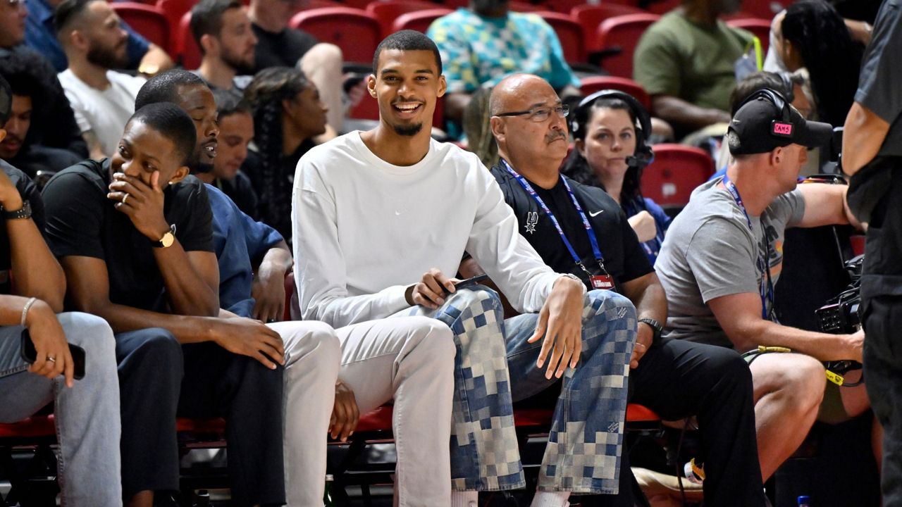 San Antonio Spurs' Victor Wembanyama, center, sits court side during the first half of an NBA summer league basketball game between the Spurs and Philadelphia 76ers, July 10, 2025, in Las Vegas. (AP Photo/David Becker)