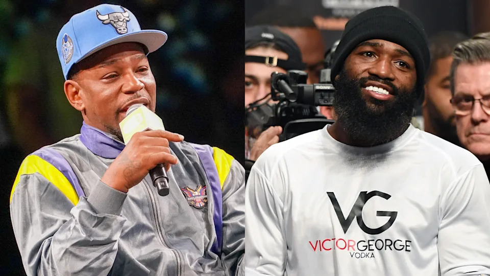 Two men side by side; one in a sports jacket and cap speaking into a microphone, the other in a white shirt smiling.