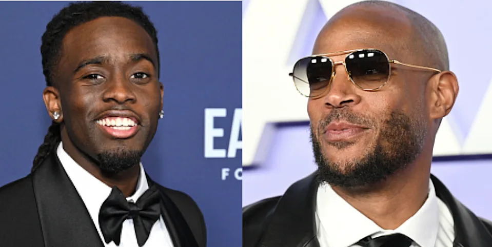 Two men in formal attire at an event. The man on the left wears a black tuxedo and the man on the right wears sunglasses and a leather jacket.