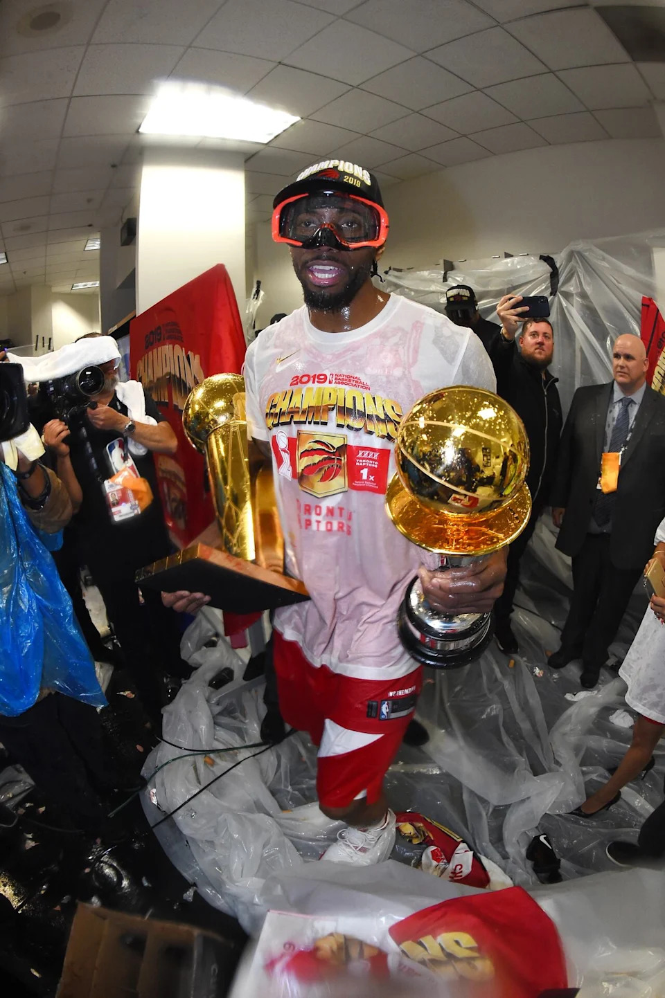 Kawhi Leonard celebrates the Toronto Raptors' 2019 NBA championship while holding the Larry O'Brien Championship Trophy and the Bull Russell NBA Finals MVP Award.