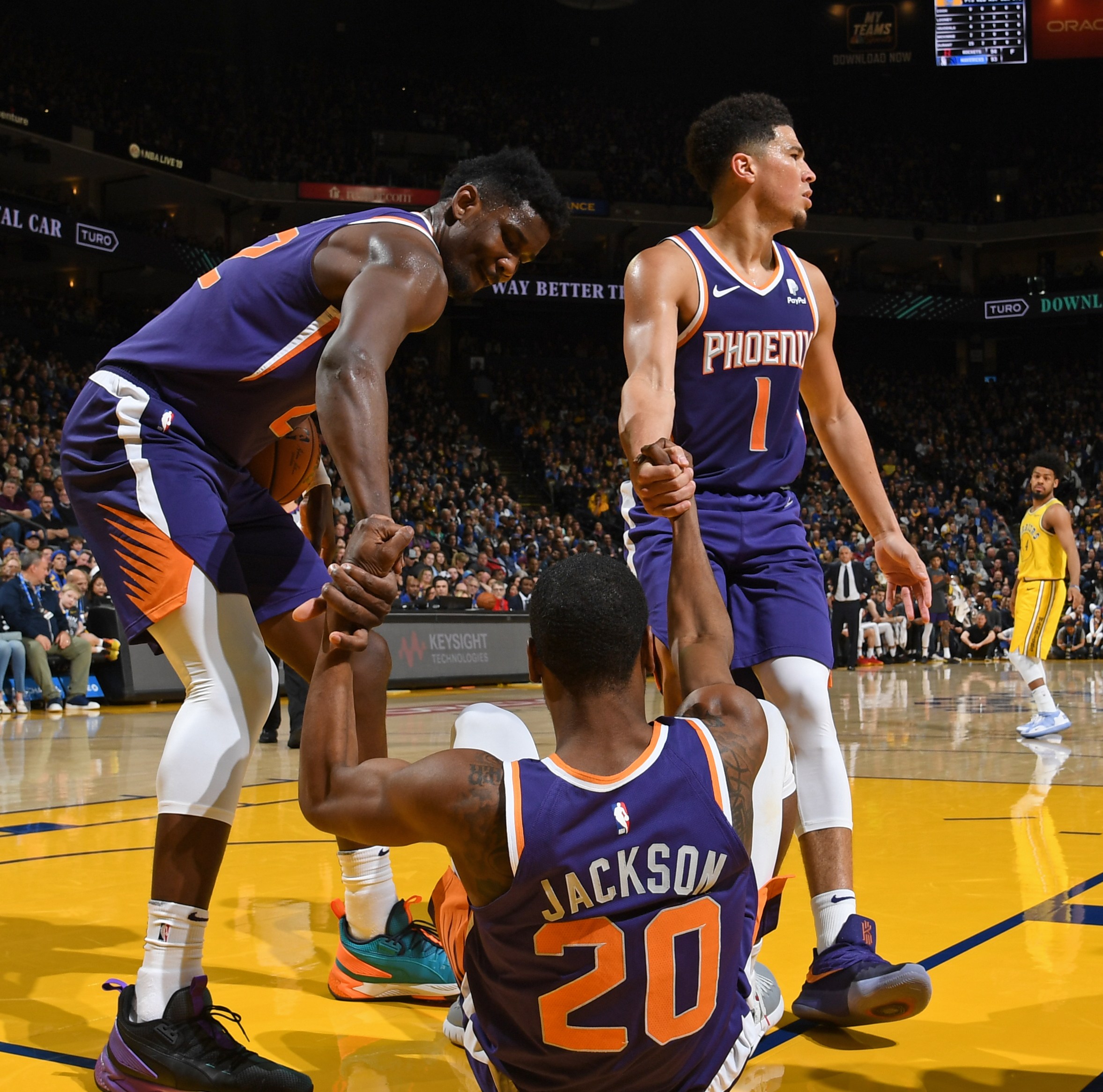 OAKLAND, CA - MARCH 10: Deandre Ayton #22, and Devin Booker #1 of the Phoenix Suns help up Josh Jackson #20 of the Phoenix Suns during the game Golden State Warriors on March 10, 2019 at ORACLE Arena in Oakland, California. NOTE TO USER: User expressly acknowledges and agrees that, by downloading and or using this photograph, user is consenting to the terms and conditions of Getty Images License Agreement. Mandatory Copyright Notice: Copyright 2019 NBAE (Photo by Noah Graham/NBAE via Getty Images)