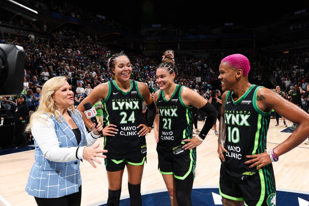 A reporter with an ESPN microphone interviews three Minnesota Lynx players, wearing black and neon green jerseys, on a basketball court.