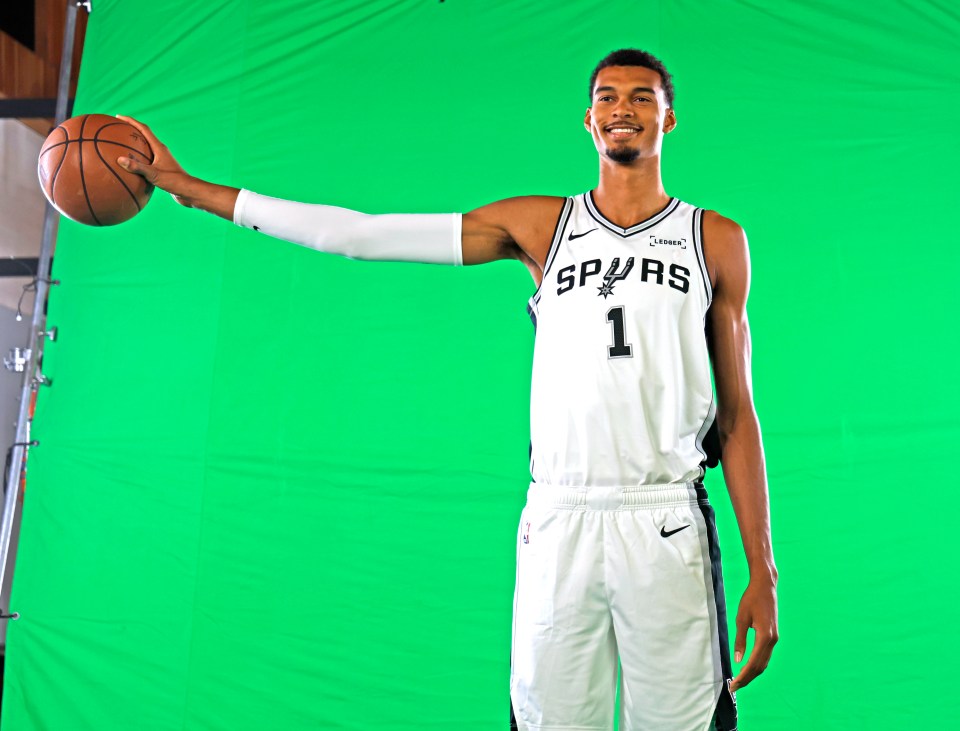 Victor Wembanyama holds a basketball with his right arm extended to show off his wingspan