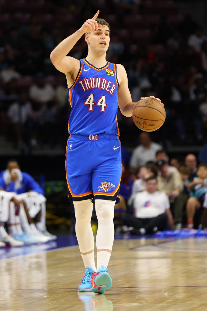 A Thunder player with number 44 on his jersey is holding a basketball and pointing his finger up, looking determined.