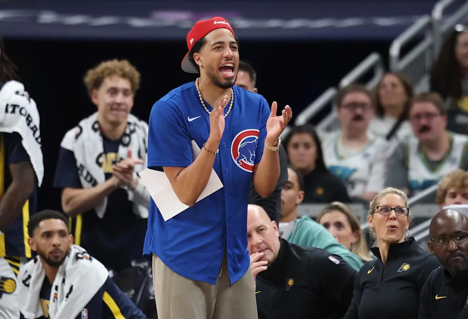 Tyrese Haliburton cheers and claps in front of the Pacers bench. He is wearing a Cubs jersey and backwards cap.