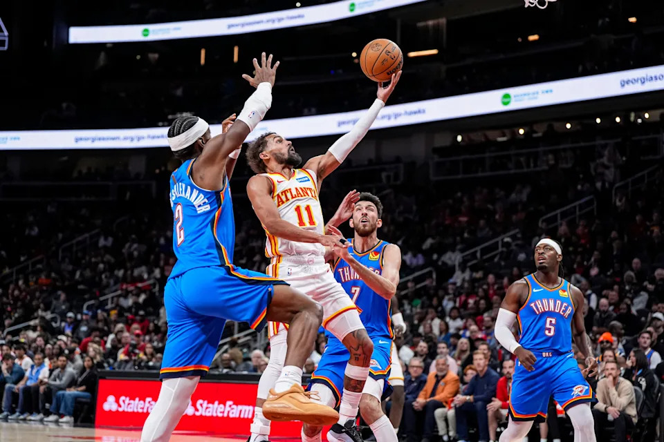 Oct 25, 2025; Atlanta, Georgia, USA; Atlanta Hawks guard Trae Young (11) goes to the basket between Oklahoma City Thunder guard Shai Gilgeous-Alexander (2) and center Chet Holmgren (7) during the first half at State Farm Arena. Mandatory Credit: Dale Zanine-Imagn Images