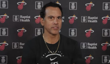 Miami Head Coach Erik Spoelstra Speaks to media. He is wearing gold chain and black long sleeve. He is standing in front of Miami Heat and Baptist Health screen.