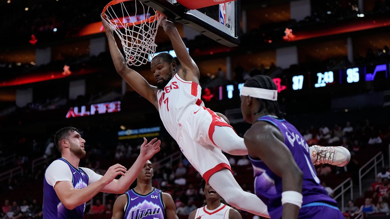 Houston Rockets forward Kevin Durant (7) hangs from the hoop after dunking during the first half of an NBA basketball preseason game against the Utah Jazz in Houston, Wednesday, Oct. 8, 2025. (AP Photo/Ashley Landis)