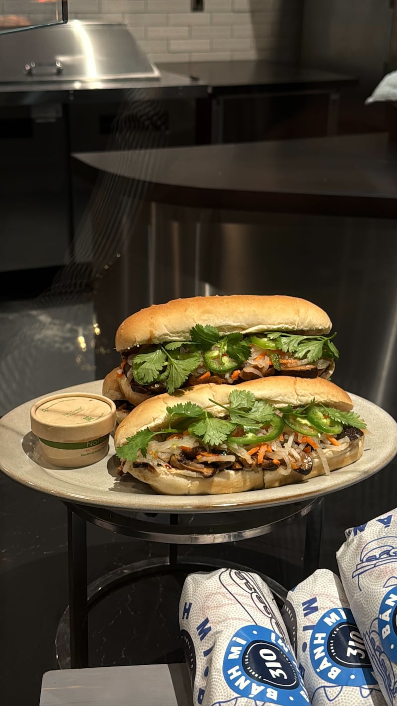 A close-up of a mushroom banh mi sandwich on a tray at the Intuit Dome, with marinated mushrooms, pickled vegetables, and fresh cilantro inside a toasted baguette.