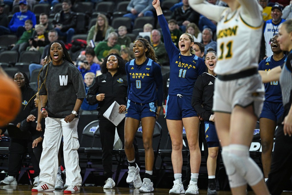 The Kansas City women's basketball coaches and players on the bench celebrate a big play during the 2025 Summit League Tournament. 