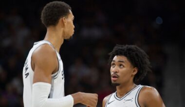 San Antonio Spurs center Victor Wembanyama, left, speaks with teammate Dylan Harper, right, during the first half of a preseason NBA basketball game against the Utah Jazz, Friday, Oct. 10, 2025, in San Antonio. (AP Photo/Darren Abate)