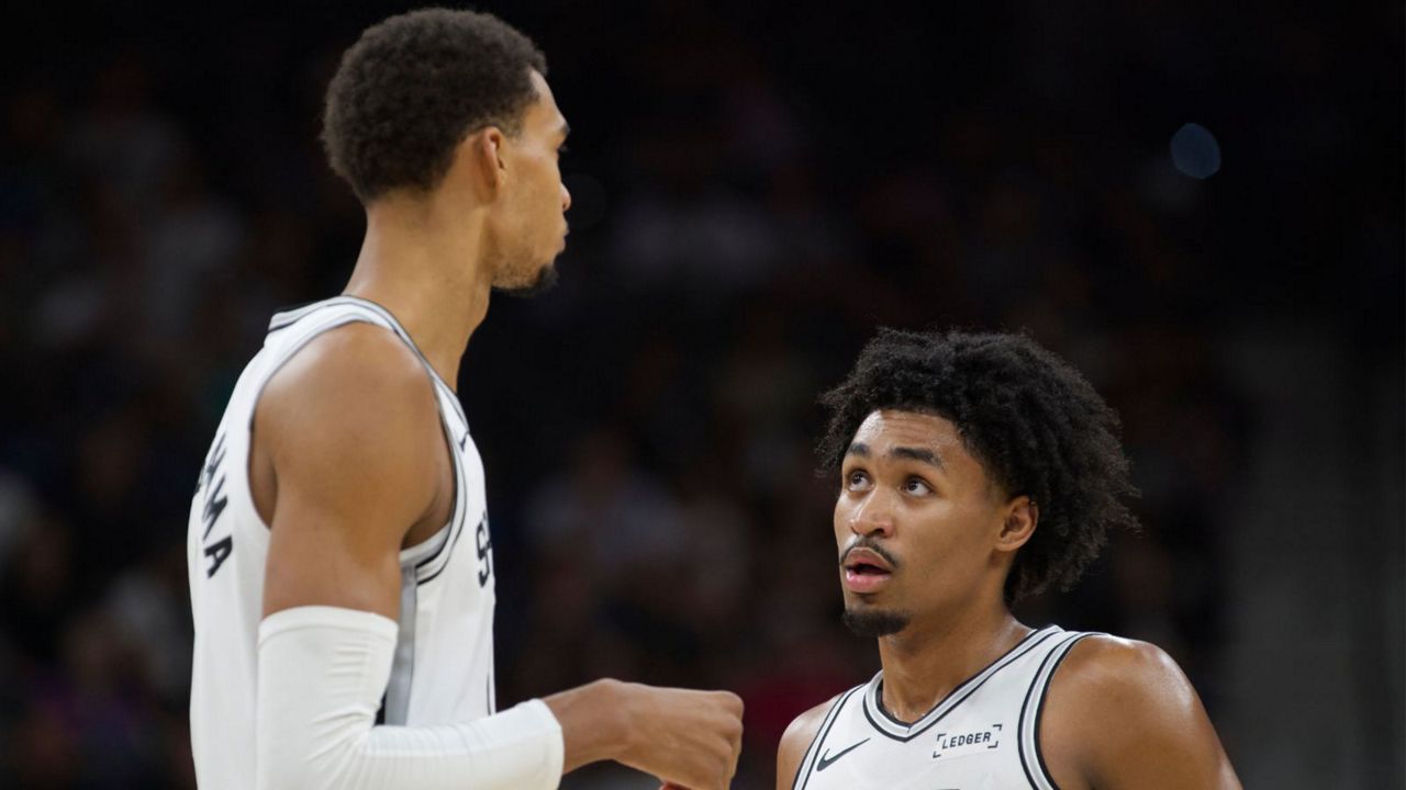 San Antonio Spurs center Victor Wembanyama, left, speaks with teammate Dylan Harper, right, during the first half of a preseason NBA basketball game against the Utah Jazz, Friday, Oct. 10, 2025, in San Antonio. (AP Photo/Darren Abate)