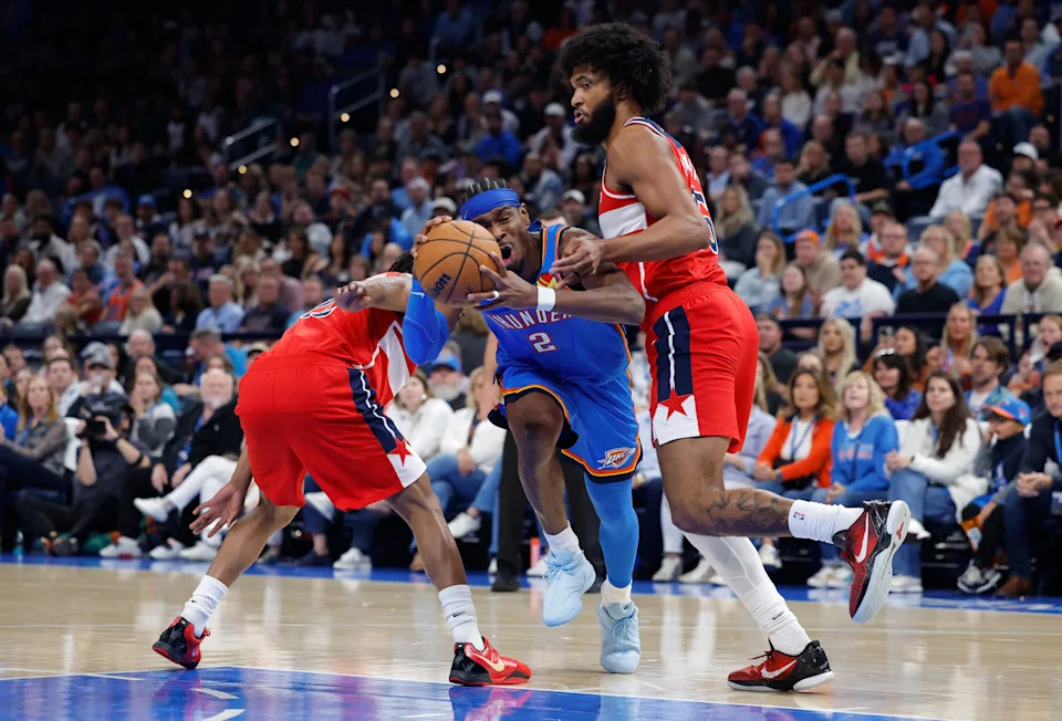 Oct 30, 2025; Oklahoma City, Oklahoma, USA; Oklahoma City Thunder guard Shai Gilgeous-Alexander (2) drives between Washington Wizards guard Tre Johnson (12) and forward Marvin Bagley III (35) during the second half at Paycom Center. Mandatory Credit: Alonzo Adams-Imagn Images