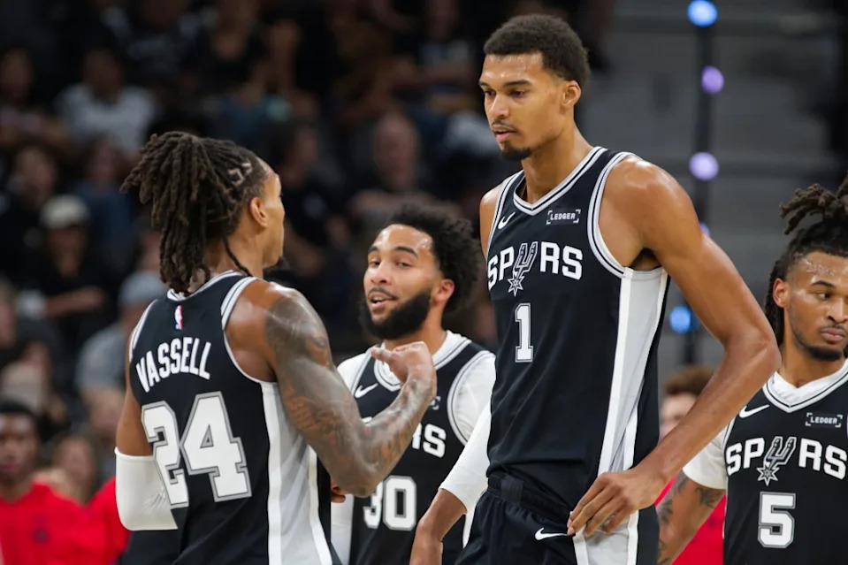 San Antonio Spurs center Victor Wembanyama (1) speaks with Spurs guard Devin Vassell (24) during the first half of their NBA basketball game against the Toronto Raptors, Monday, Oct. 27, 2025, in San Antonio. (AP Photo/Darren Abate)