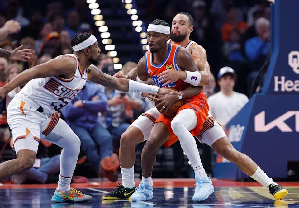 Nov 28, 2025; Oklahoma City, Oklahoma, USA; Oklahoma City Thunder guard Shai Gilgeous-Alexander (2) is defended by Phoenix Suns guard Jordan Goodwin (23) and forward Dillon Brooks (3) during the second quarter at Paycom Center. Mandatory Credit: Alonzo Adams-Imagn Images