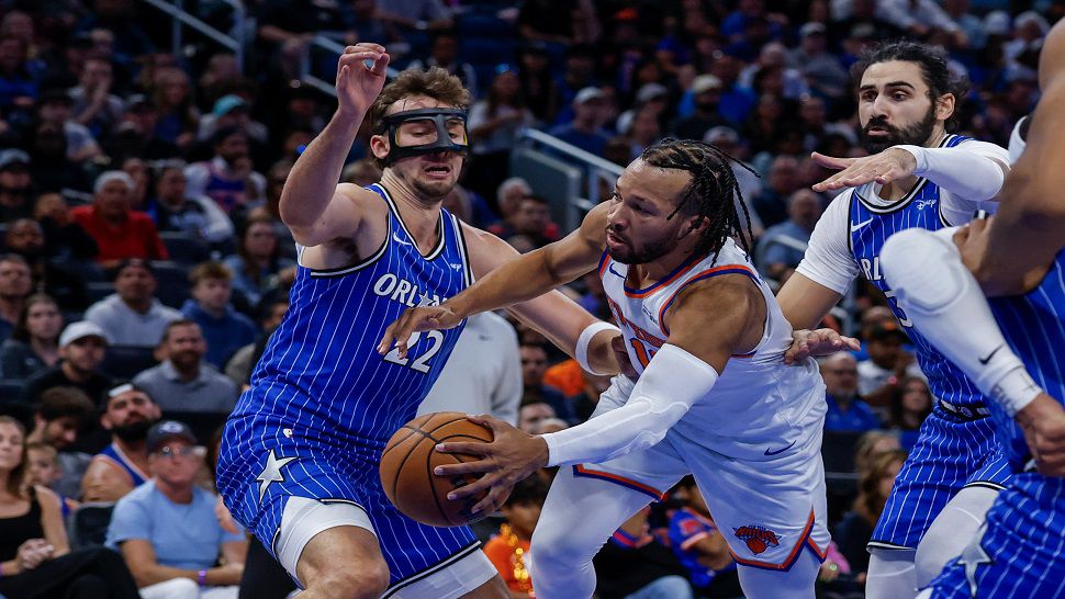 New York Knicks guard Jalen Brunson, right, passes the ball around Orlando Magic forward Franz Wagner during the first half of an NBA basketball game, Saturday, Nov. 22, 2025, in Orlando, Fla. (AP Photo/Kevin Kolczynski)