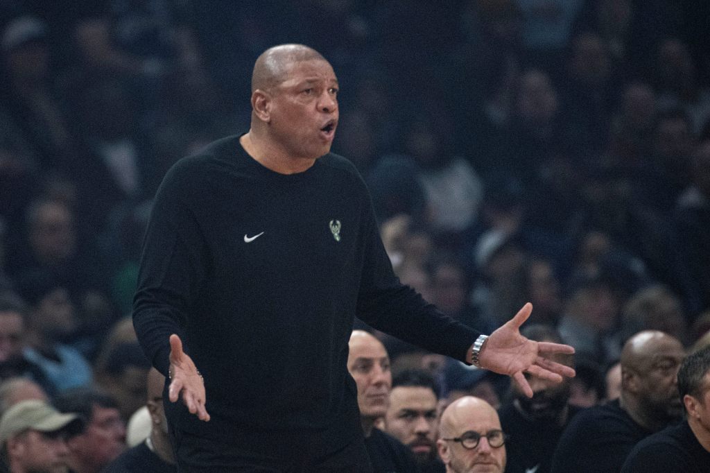 Doc Rivers on the court wearing a black long-sleeved shirt with the Bucks logo.