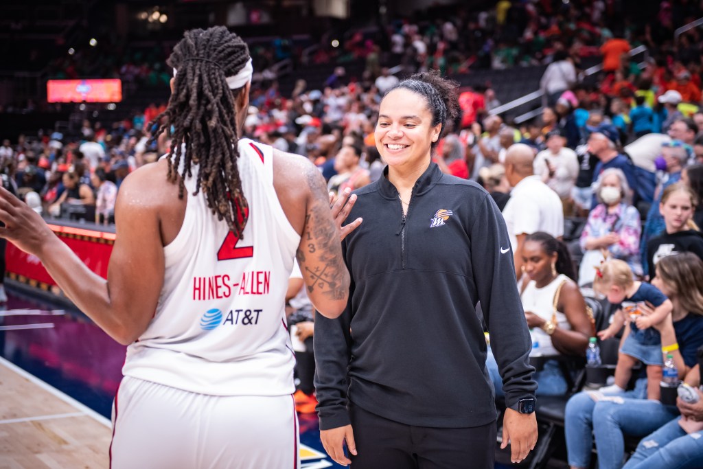 Kristi Toliver smiles while saying hello to former teammate. She is wearing a black quarter zip and black pants and facing the camera. 